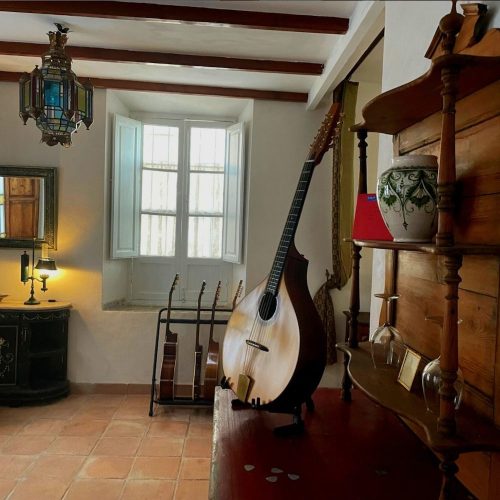 Bouzouki standing on an old dresser in an old house with guitars in the background.